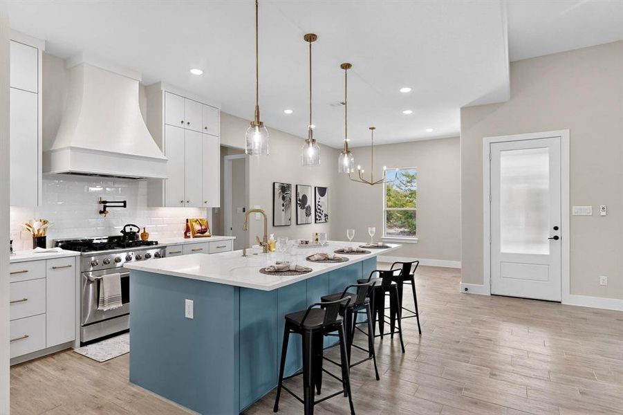 Kitchen featuring white cabinets, a large island, custom exhaust hood, a breakfast bar area, and gas range