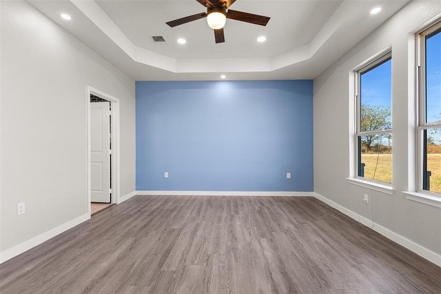 Empty room featuring a raised ceiling, wood finished floors, recessed lighting, and a ceiling fan