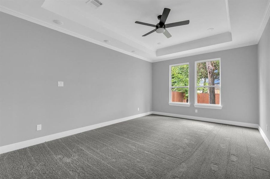 Empty room with ceiling fan, a raised ceiling, crown molding, and carpet flooring