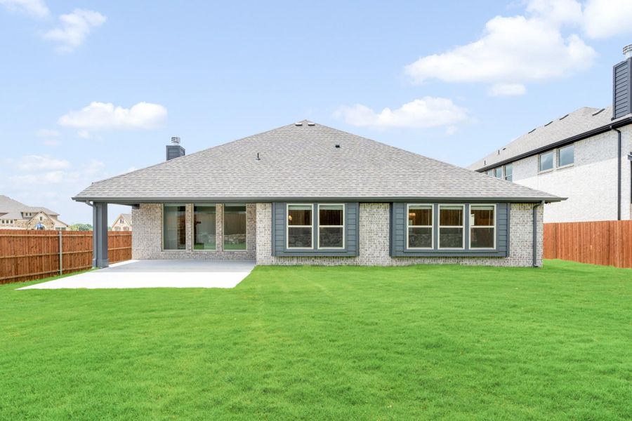 Rear view of single-story brick home with covered patio, large windows, and fenced green backyard Rear view of single-story brick home with covered patio, large windows, and fenced green backyard