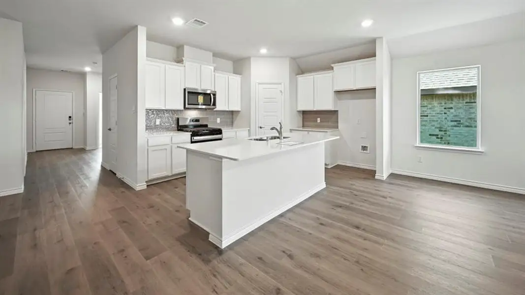 Open-concept kitchen featuring an island with a sink, white cabinetry, stainless steel microwave, and wood-finish flooring Open-concept kitchen featuring an island with a sink, white cabinetry, stainless steel microwave, and wood-finish flooring