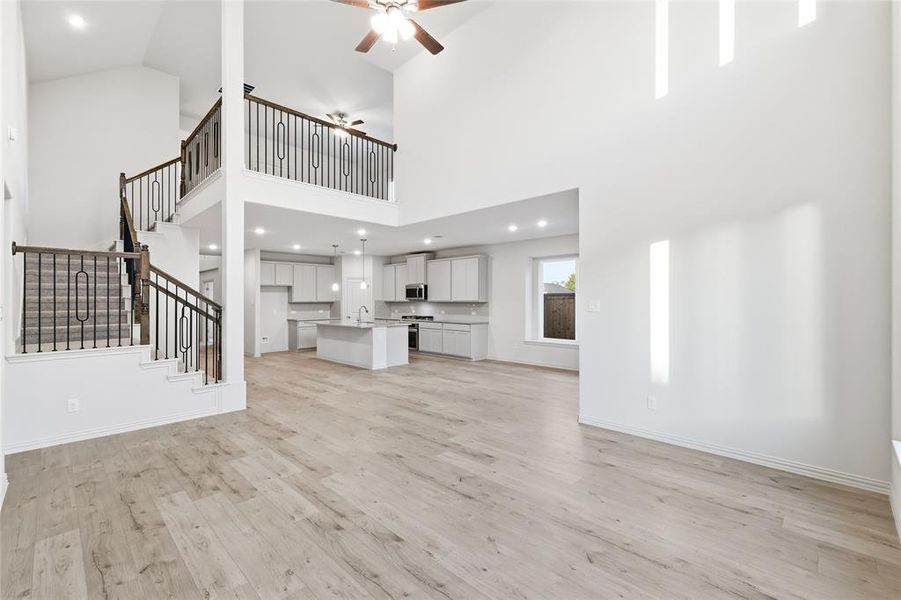 Unfurnished living room with light wood finished floors, ceiling fan, stairway, recessed lighting, and a high ceiling