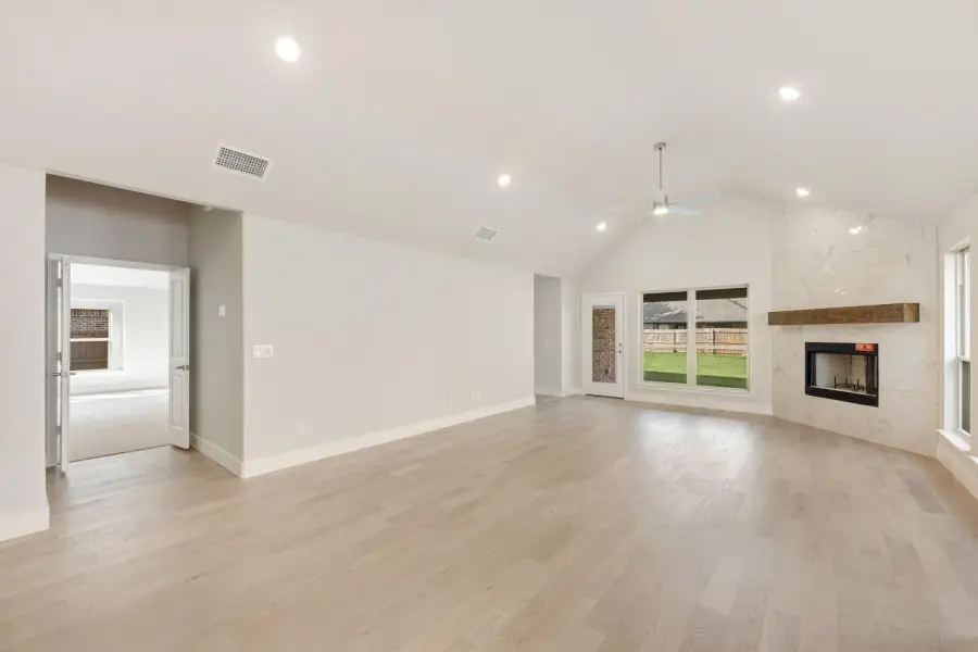 Open living room with vaulted ceiling, light hardwood floors, ceiling fan, and stone fireplace with wood mantel
