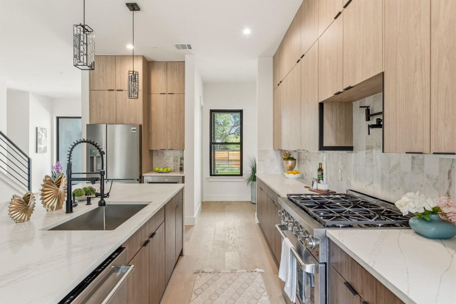 Modern kitchen featuring light wood-finish cabinetry, white stone countertops, a stainless steel gas range, and a full-height stone backsplash