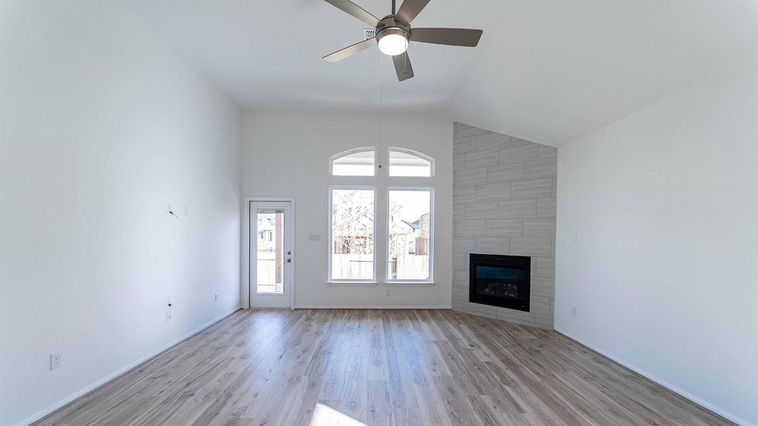 Unfurnished living room with light wood finished floors, vaulted ceiling, a large fireplace, and ceiling fan