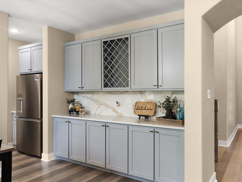 Bar featuring gray cabinetry, stainless steel fridge, light stone countertops, decorative backsplash, and dark wood-style flooring