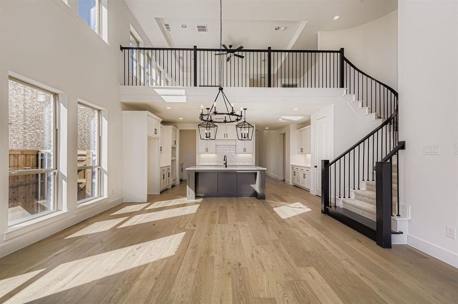 Unfurnished living room with a chandelier, healthy amount of natural light, light wood finished floors, a high ceiling, and stairs