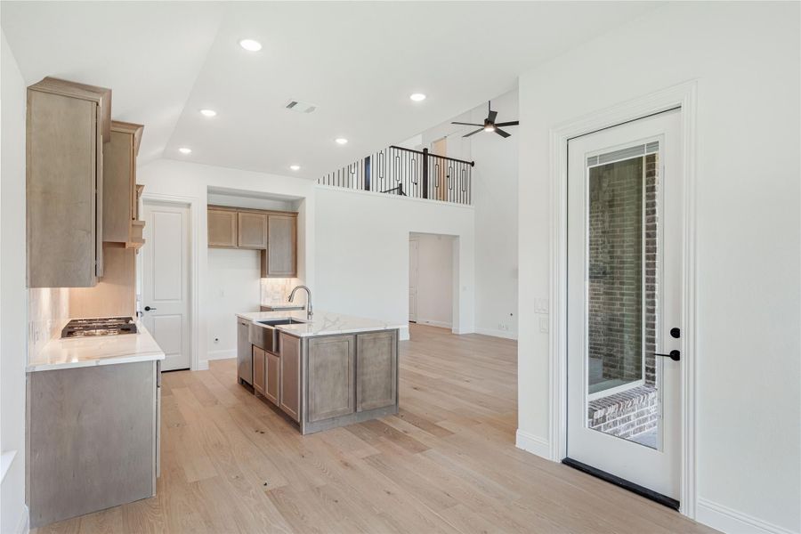 Open kitchen with center island, wood cabinets, light hardwood floors, and two-story ceiling with upper balcony