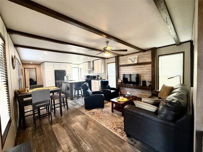 Living room featuring beam ceiling, dark wood-type flooring, a ceiling fan, and wood walls