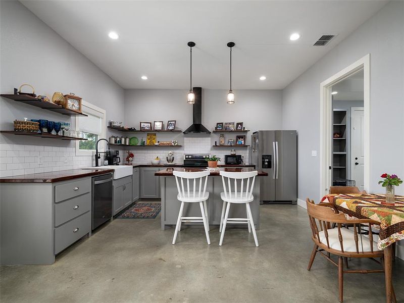 Kitchen featuring gray cabinetry, stainless steel appliances, a kitchen bar, wood counters, and open shelves Kitchen featuring gray cabinetry, stainless steel appliances, a kitchen bar, wood counters, and open shelves