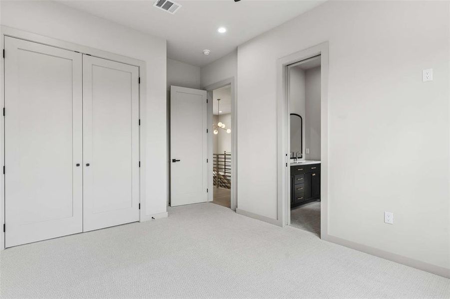 Light-toned wall-to-wall carpeting in a room featuring two white panel doors with black hardware, recessed ceiling lighting, and a white baseboard trim. Light-toned wall-to-wall carpeting in a room featuring two white panel doors with black hardware, recessed ceiling lighting, and a white baseboard trim.