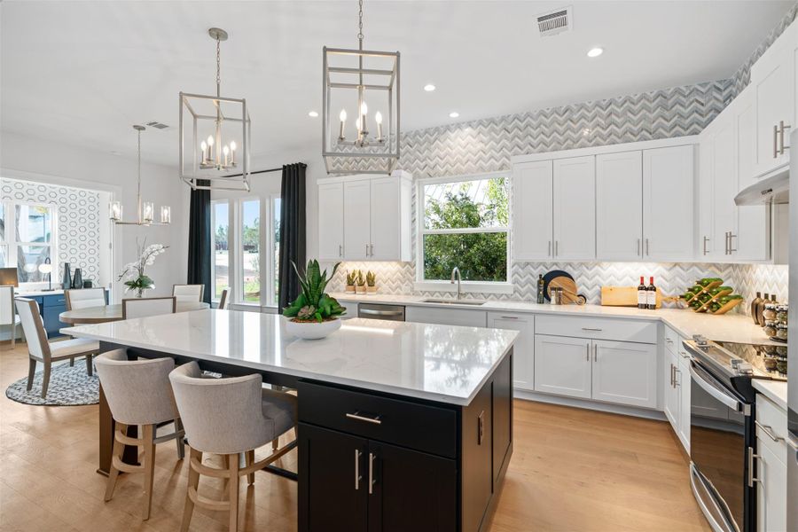 Kitchen with electric range oven, white cabinetry, dark cabinets, a chandelier, and recessed lighting. The photos shown are of a completed home with the same floor plan and may not reflect the exact finishes, features, or layout of the home currently under construction.