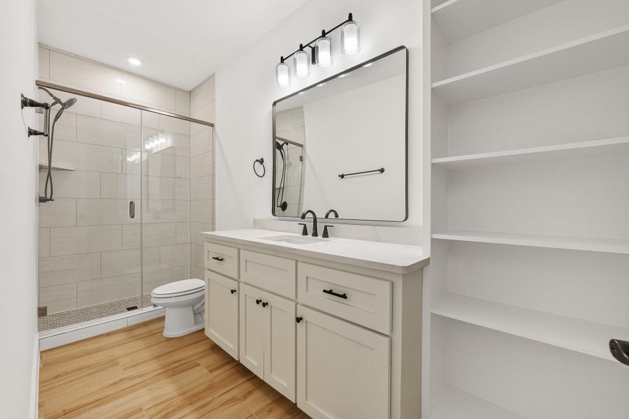 This secondary bathroom featuring a glass-enclosed shower, a large vanity with ample storage, and built-in shelving. The space is bright with elegant fixtures and wood-style flooring. This secondary bathroom featuring a glass-enclosed shower, a large vanity with ample storage, and built-in shelving. The space is bright with elegant fixtures and wood-style flooring.