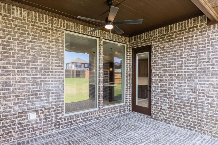 Covered brick patio with ceiling fan, large window, and glass door leading to backyard Covered brick patio with ceiling fan, large window, and glass door leading to backyard