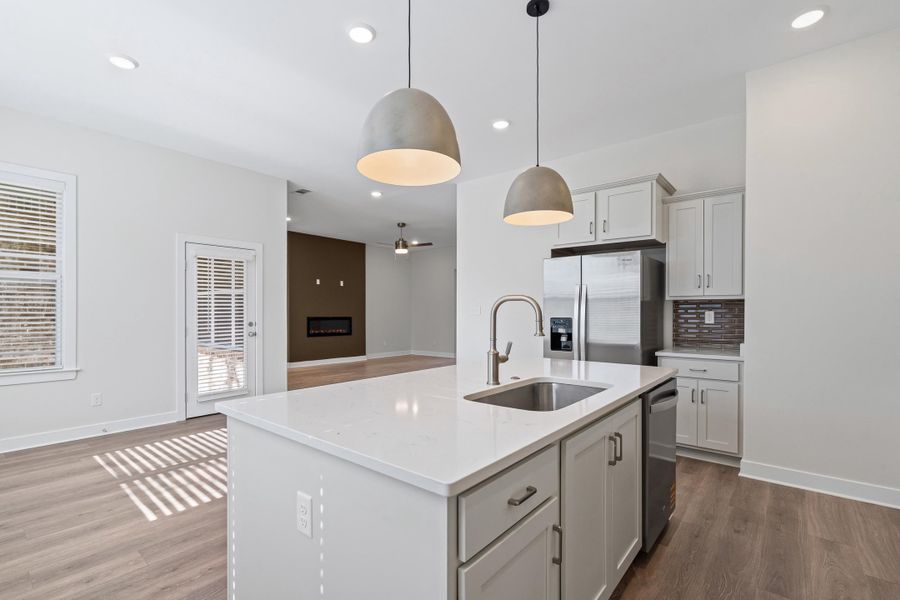 Kitchen featuring a center island with sink, light stone countertops, decorative light fixtures, stainless steel appliances, and open floor plan
