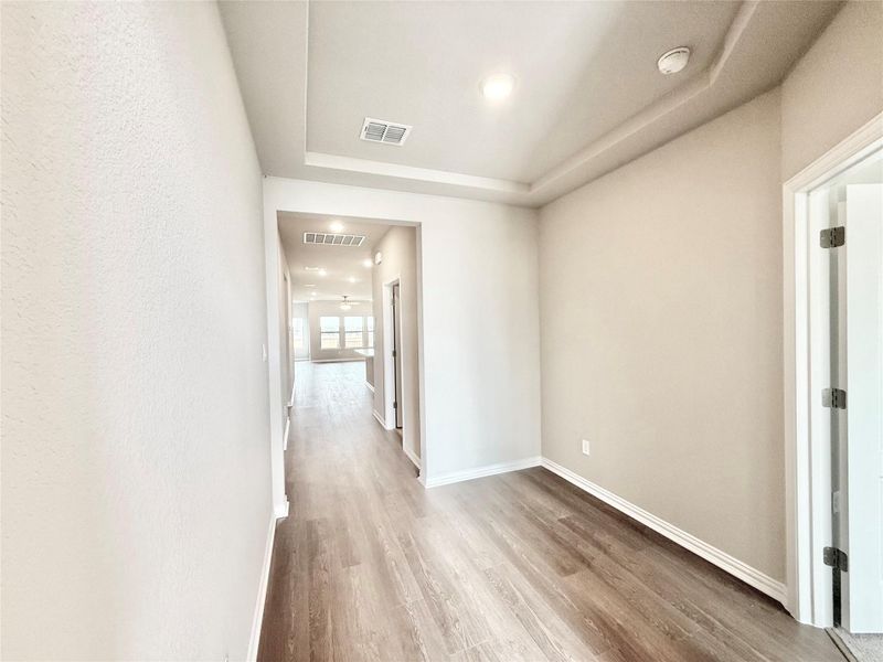 Hallway featuring light wood-style floors, a tray ceiling, and recessed lighting Hallway featuring light wood-style floors, a tray ceiling, and recessed lighting