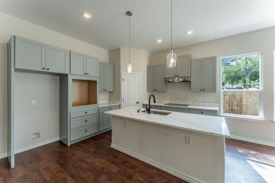 Modern kitchen featuring a central island with a waterfall-edge countertop, grey shaker-style cabinetry, dark wood-finish flooring, recessed lighting, and pendant light fixtures