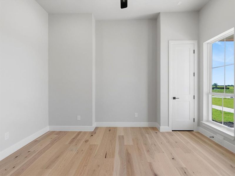 Spacious interior room featuring wood-finish flooring, white baseboards, and light gray wall tones