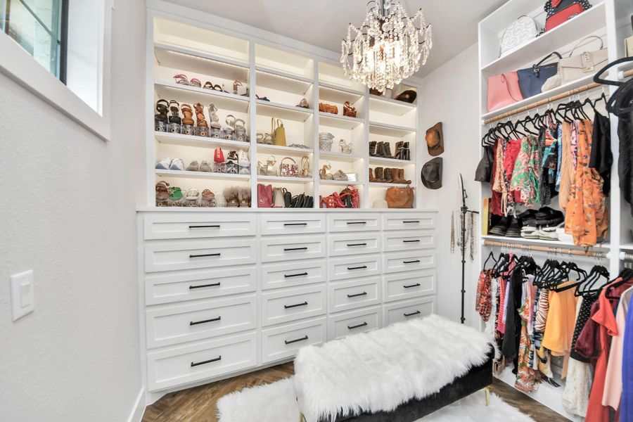 Luxurious walk-in closet featuring elegant built-in shelving, ample drawer space, and a chic chandelier, perfect for organizing and showcasing your wardrobe.