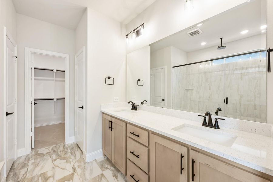 Master bathroom with double vanity, quartz countertop, large mirror, glass shower, and walk-in closet entry