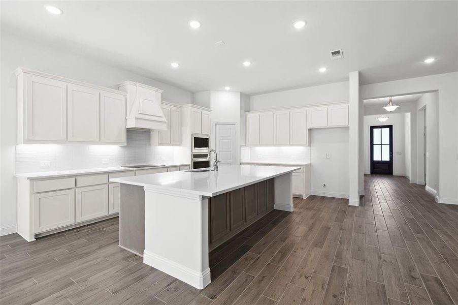 Kitchen featuring tasteful backsplash, white cabinetry, recessed lighting, an island with sink, and a kitchen bar Kitchen featuring tasteful backsplash, white cabinetry, recessed lighting, an island with sink, and a kitchen bar