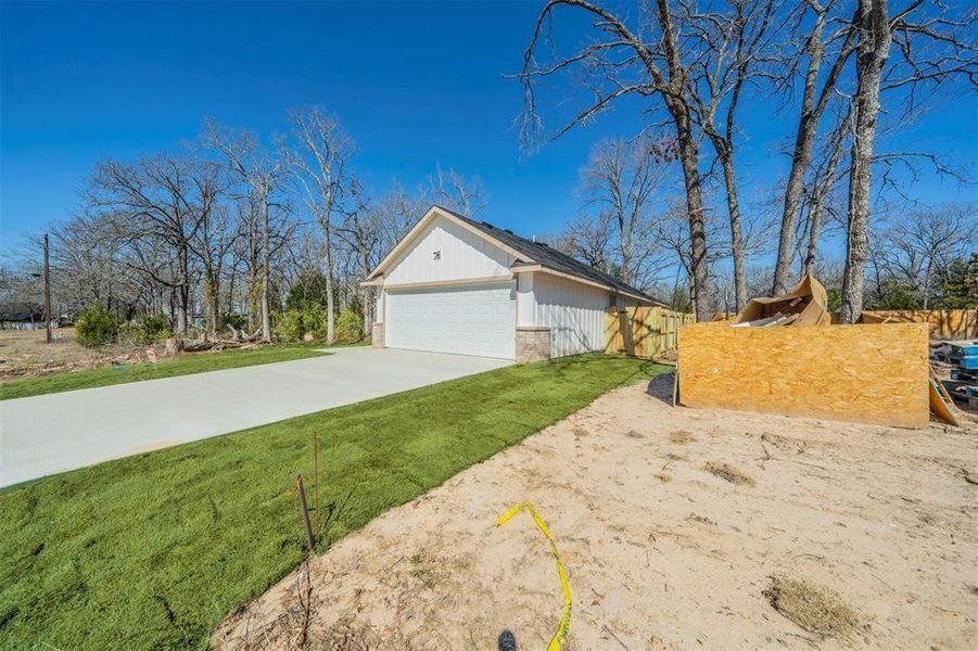 View of home's exterior with driveway, a garage, a lawn, fence, and brick siding