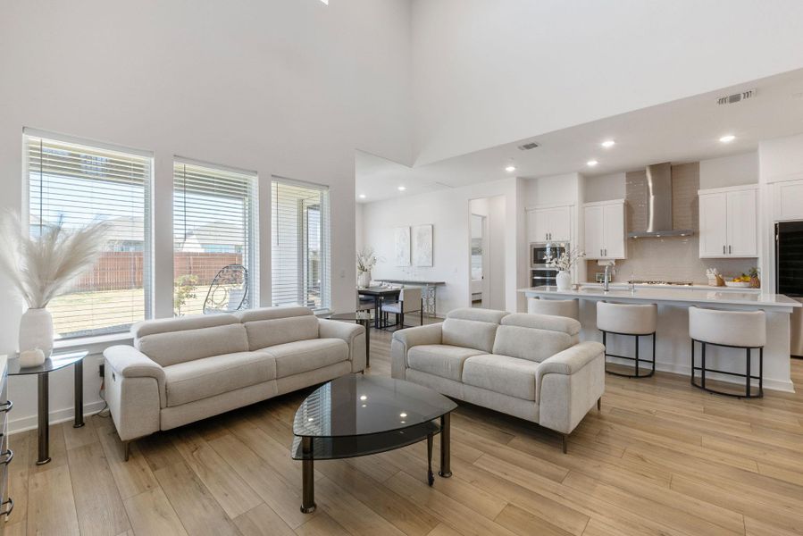 Living area featuring light wood-style flooring, recessed lighting, visible vents, and a towering ceiling