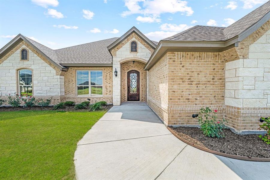 Property entrance with brick siding, stone siding, a shingled roof, and a yard