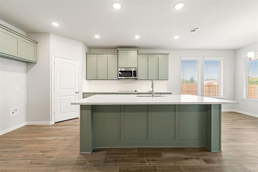 Kitchen with green cabinetry, decorative backsplash, a kitchen island with sink, and recessed lighting Kitchen with green cabinetry, decorative backsplash, a kitchen island with sink, and recessed lighting