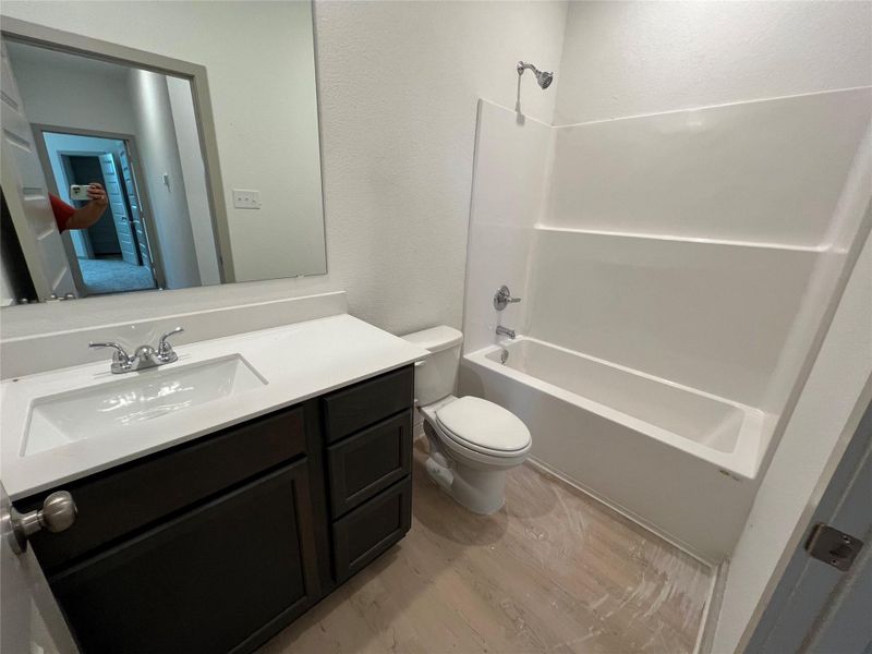 Full bathroom with shower combination, a textured wall, vanity, and light wood-style flooring Full bathroom with shower combination, a textured wall, vanity, and light wood-style flooring