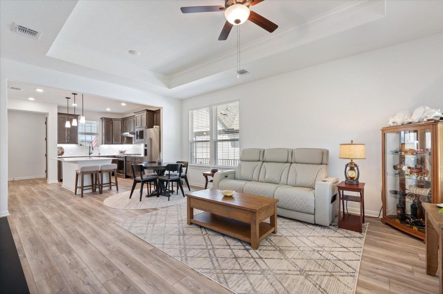 Living room with a tray ceiling, light wood-style floors, and a ceiling fan Living room with a tray ceiling, light wood-style floors, and a ceiling fan