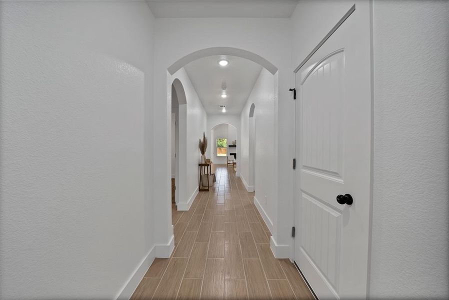 Hall with wood finish floors, arched walkways, recessed lighting, and a textured wall