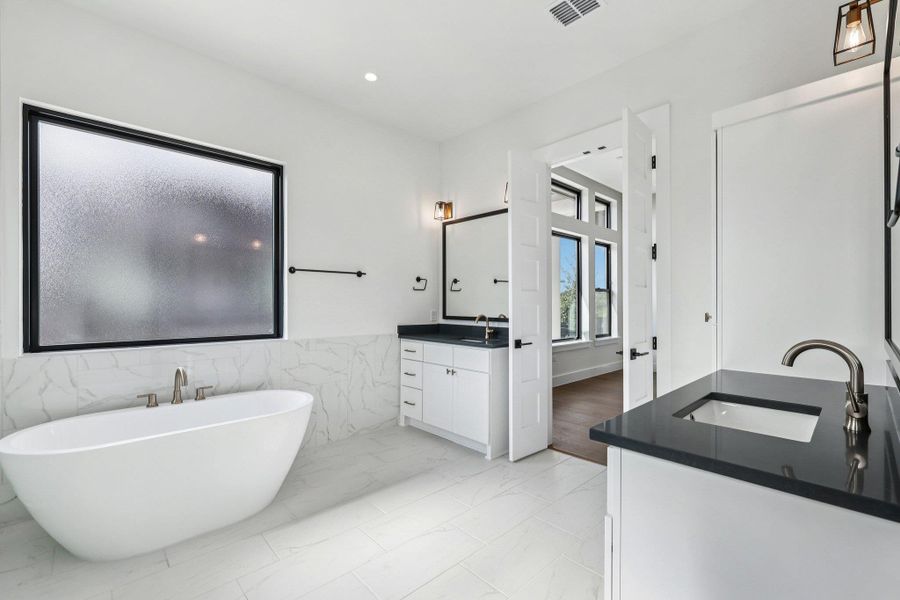 Full bath featuring a freestanding tub, two vanities, tile walls, light marble finish floors, and recessed lighting