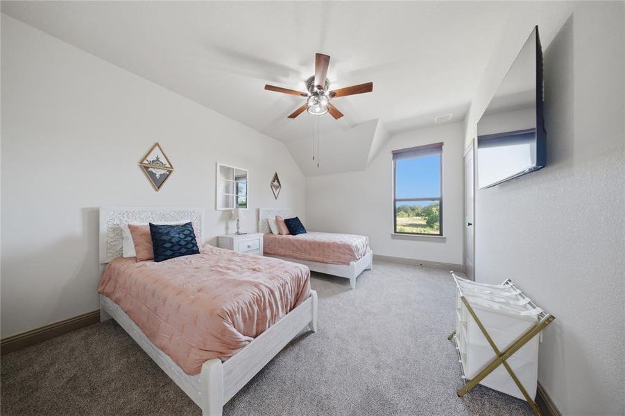 Spacious room with sloped ceilings, a ceiling fan, and light-colored carpet flooring