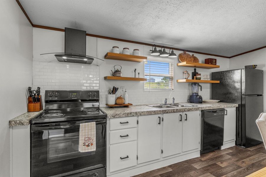 Kitchen with white cabinets, tasteful backsplash, black appliances, crown molding, and light countertops