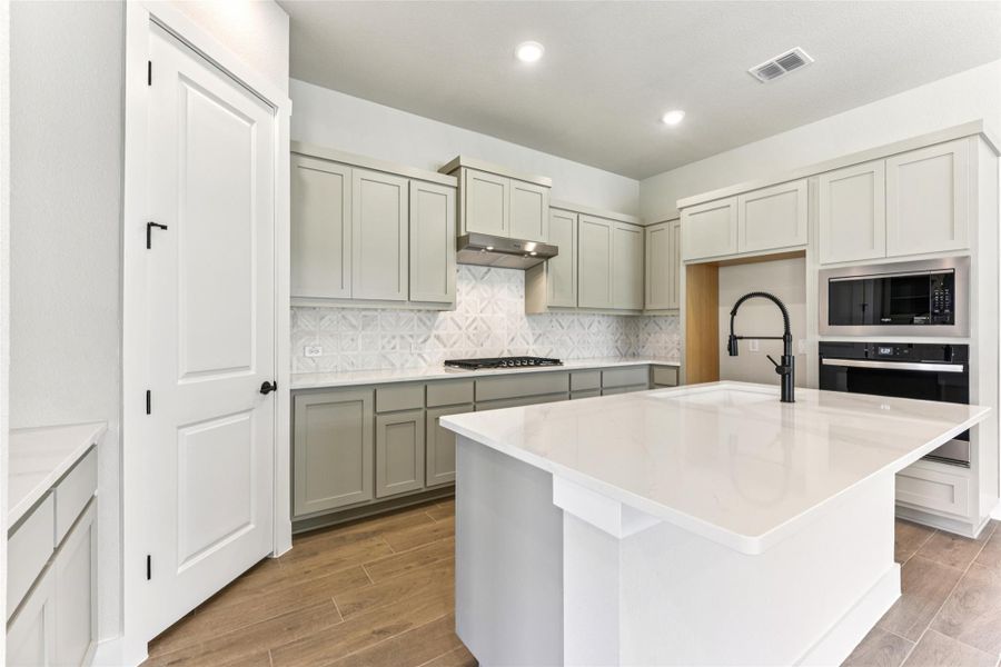Kitchen featuring decorative backsplash, oven, wood tiled floors, an island with sink, and light stone countertops Kitchen featuring decorative backsplash, oven, wood tiled floors, an island with sink, and light stone countertops