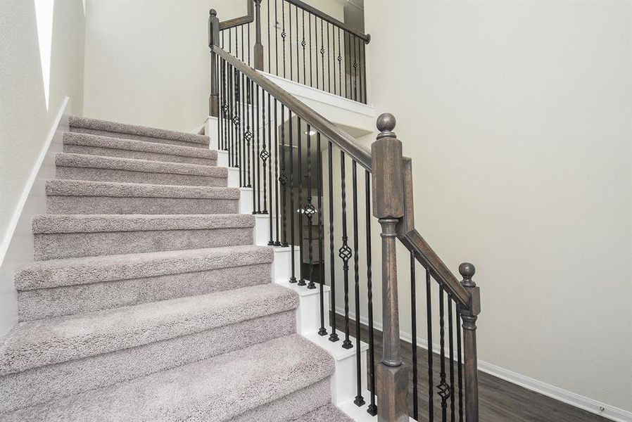 A carpeted staircase with wooden handrails and wrought-iron balusters in a clean, bright interior space.