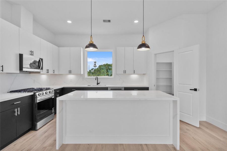 Chef-inspired kitchen showcasing an oversized waterfall island, custom cabinetry and elegant designer lighting. Chef-inspired kitchen showcasing an oversized waterfall island, custom cabinetry and elegant designer lighting.