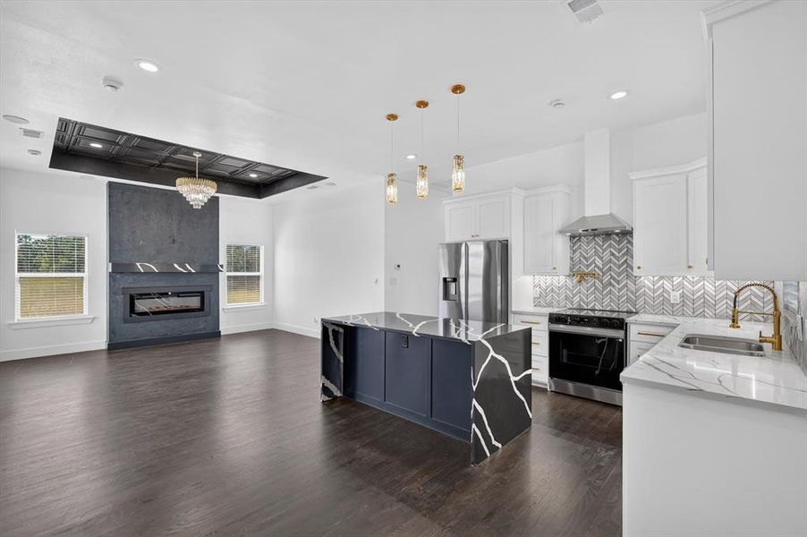 Open-concept living area featuring a kitchen island with a waterfall countertop, a linear fireplace with a stone surround, wood-finish flooring, white cabinetry, and stainless steel appliances