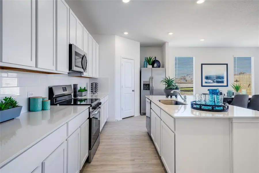 Kitchen featuring appliances with stainless steel finishes, white cabinets, light stone countertops, an island with sink, and recessed lighting