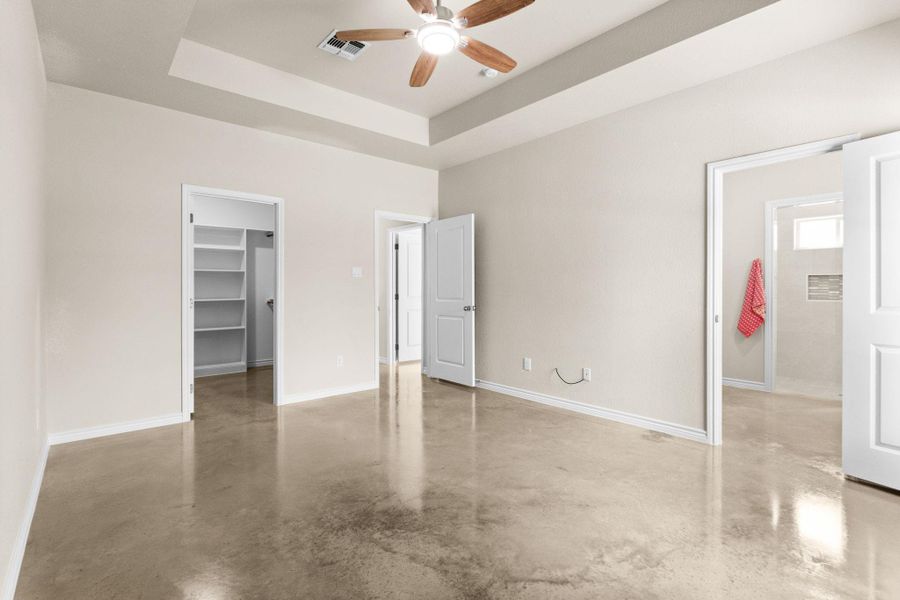 Unfurnished bedroom with a walk in closet, concrete flooring, ceiling fan, and a raised ceiling