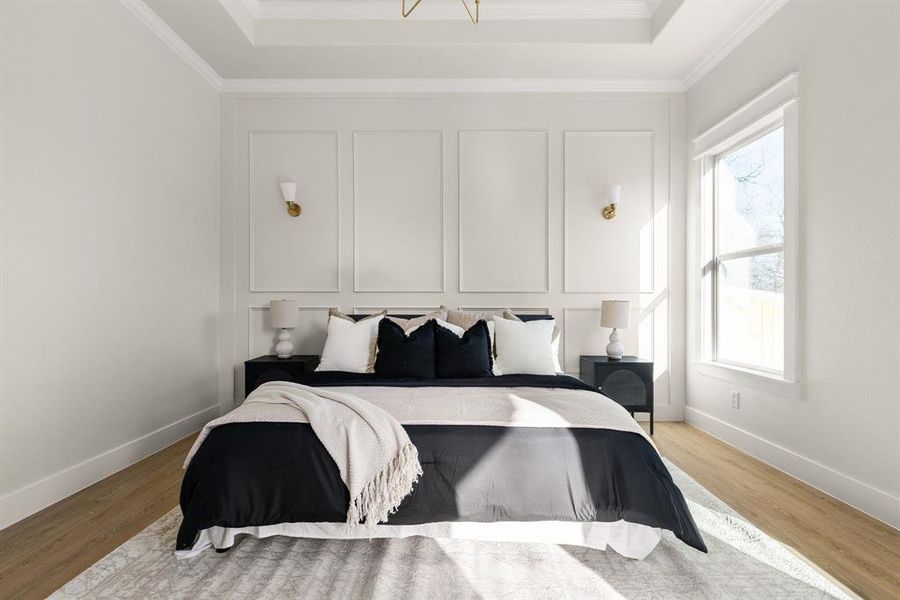 Bedroom featuring light wood-style flooring, a decorative wall, baseboards, a tray ceiling, and crown molding