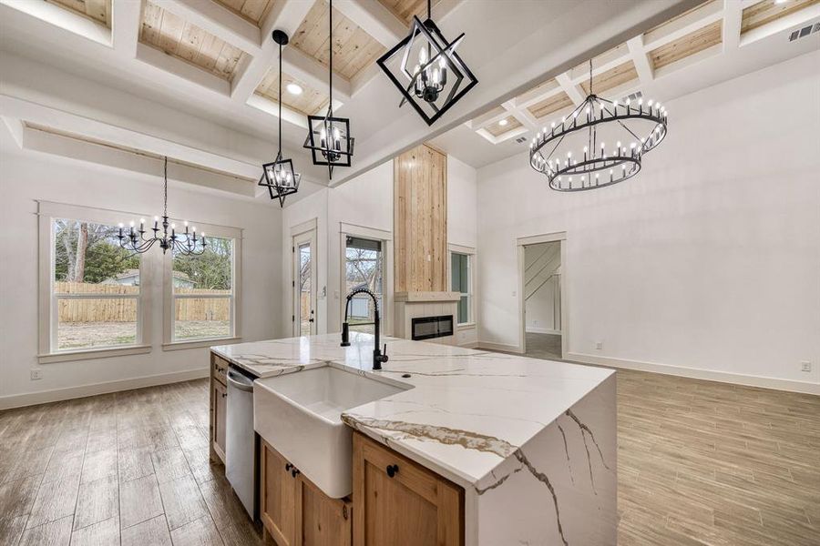 Kitchen featuring hanging lights, light wood-style flooring, an island with sink, light stone counters, and coffered ceiling