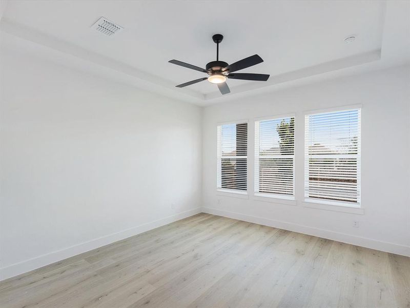 Primary Bedroom with light wood finished floors, a raised ceiling, and ceiling fan Primary Bedroom with light wood finished floors, a raised ceiling, and ceiling fan
