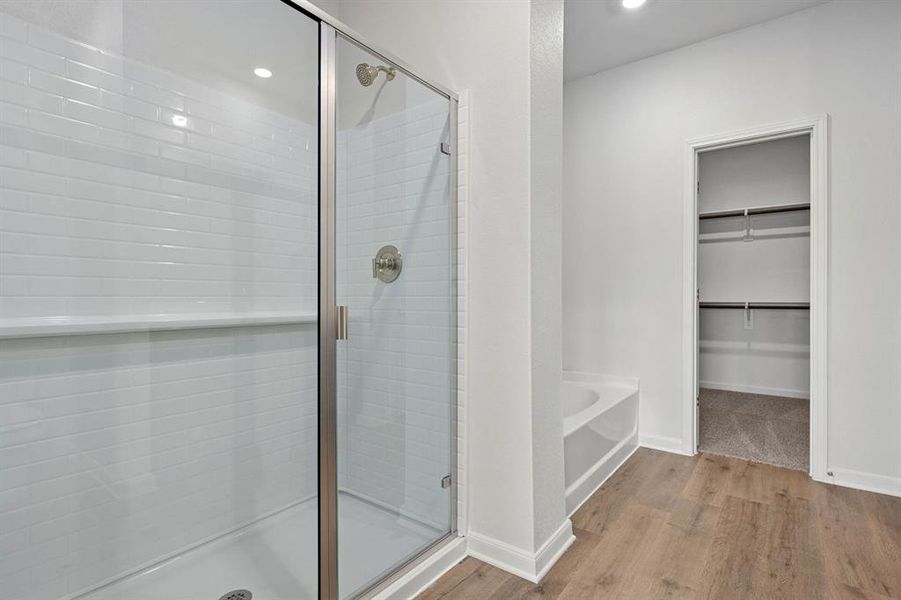 Full bathroom with light wood-style flooring, a shower stall, a garden tub, a walk in closet, and recessed lighting