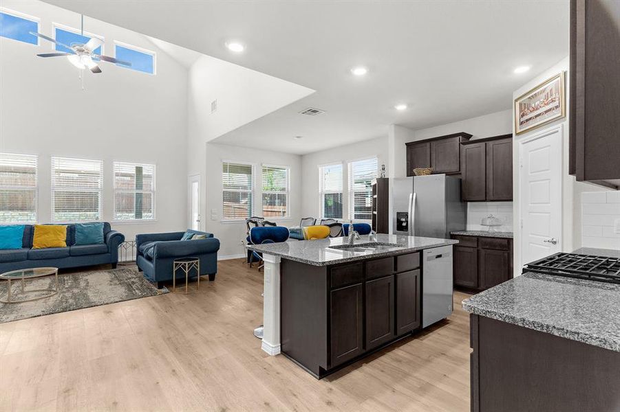 Kitchen featuring open floor plan, stainless steel appliances, visible vents, light wood-style flooring, and dark brown cabinets