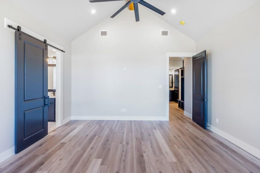 Empty room featuring a barn door, ceiling fan, high vaulted ceiling, and light wood-type flooring