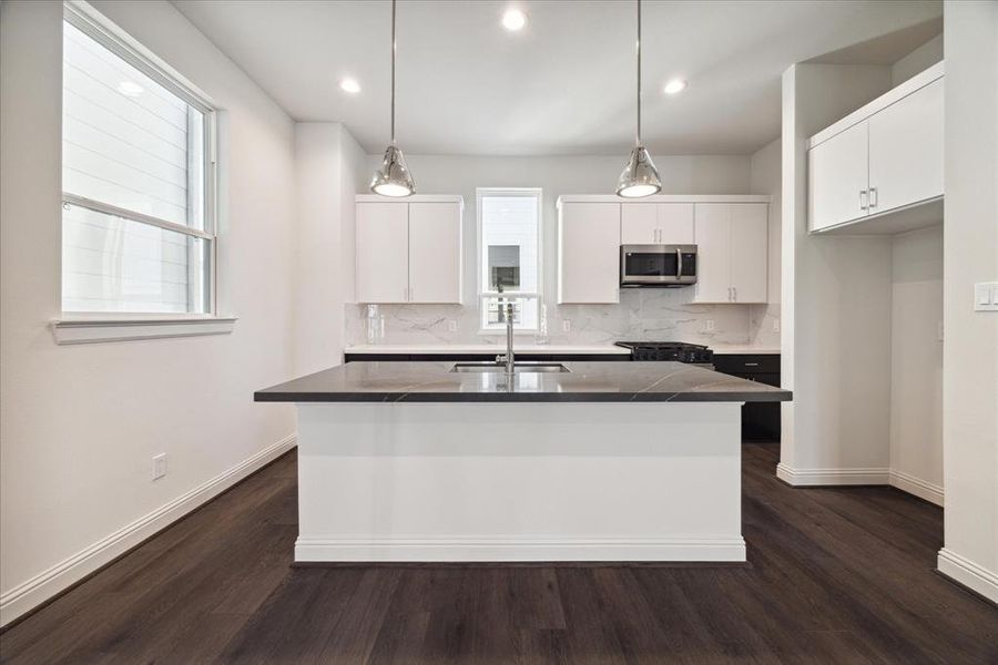 This contemporary kitchen is designed to impress, featuring crisp white cabinetry, a stylish marble-patterned backsplash, and stainless steel appliances. The oversized island with a quartz countertop provides ample workspace and doubles as a gathering spot for family and friends. Pendant lighting adds a touch of elegance, while large windows flood the space with natural light, creating an inviting atmosphere for cooking and entertaining alike.