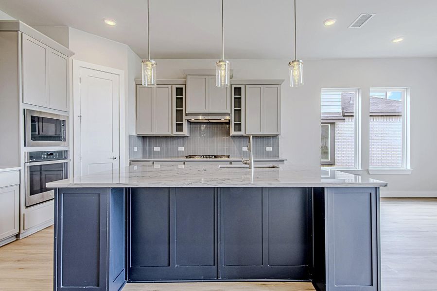 The expansive island takes center stage with its navy cabinetry, marble-style quartz counters, and trio of pendant lights that lend a modern, elegant touch. The expansive island takes center stage with its navy cabinetry, marble-style quartz counters, and trio of pendant lights that lend a modern, elegant touch.