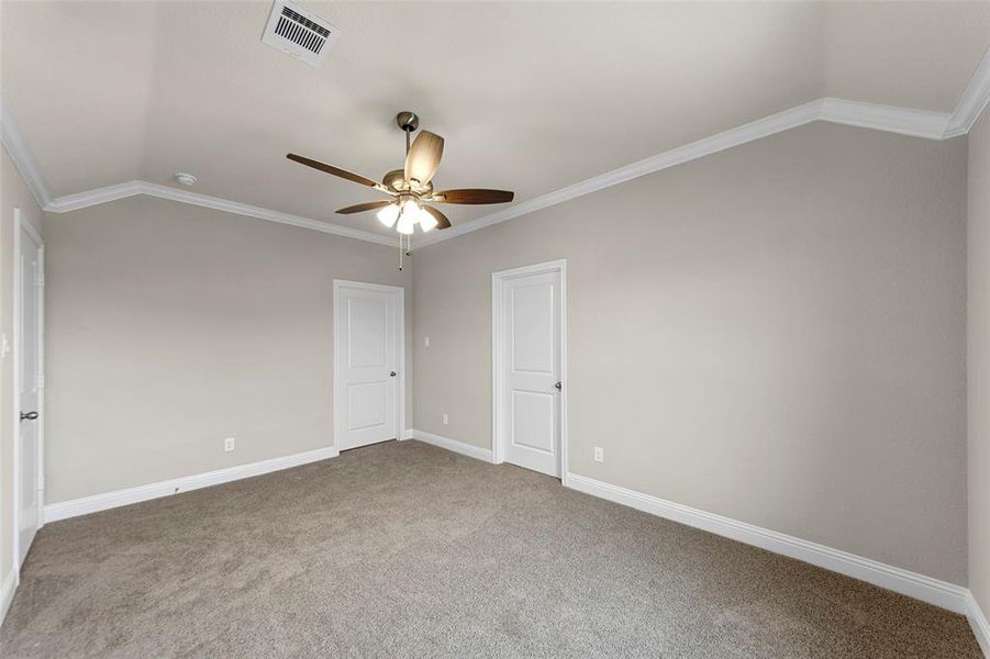 Carpeted room featuring a vaulted ceiling with crown molding, two panel doors, a ceiling fan with light kit, and neutral wall paint
